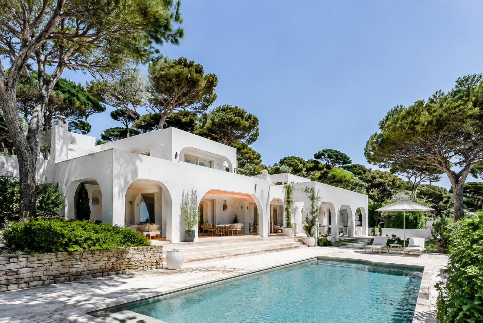 Whitewashed villa with arches and a pool beneath umbrella pines